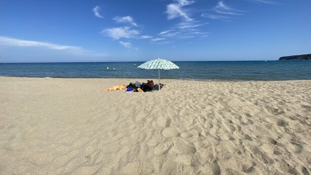 Ein Strand mit einer Person, die unter einem gemusterten Sonnenschirm liegt und aufs Meer blickt.