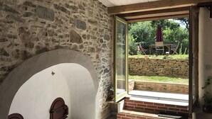 Ein Zimmer mit Steinwänden und einer großen Glasdoor zu einem Außenbereich mit Steinmauer und Grünpflanzen.