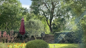 Ein Garten mit einer Steinsäule, einer Holzbank und einem roten Sonnenschirm.