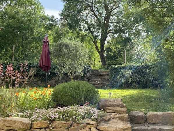 A garden with a stone wall, a wooden bench, and a red umbrella. - Renovated wine cellar and outbuildings surrounded by nature (Villetritouls)