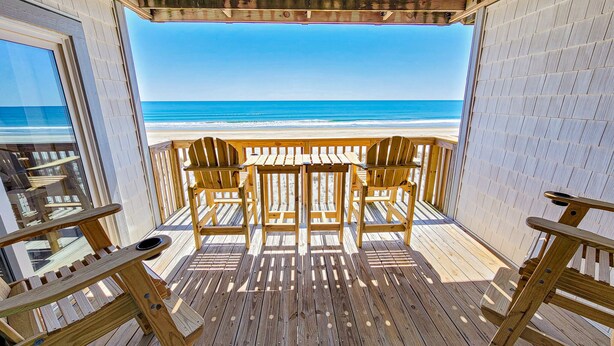 A wooden deck with a view of the beach and ocean.
