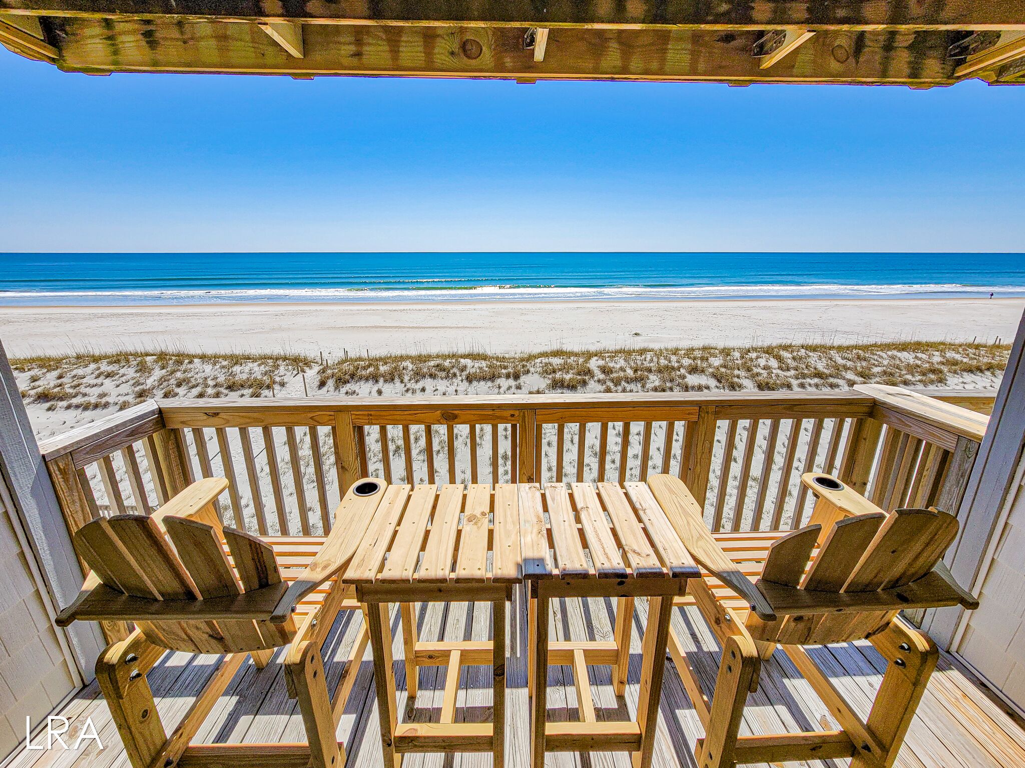 A wooden deck with a table and chairs overlooking a beach.