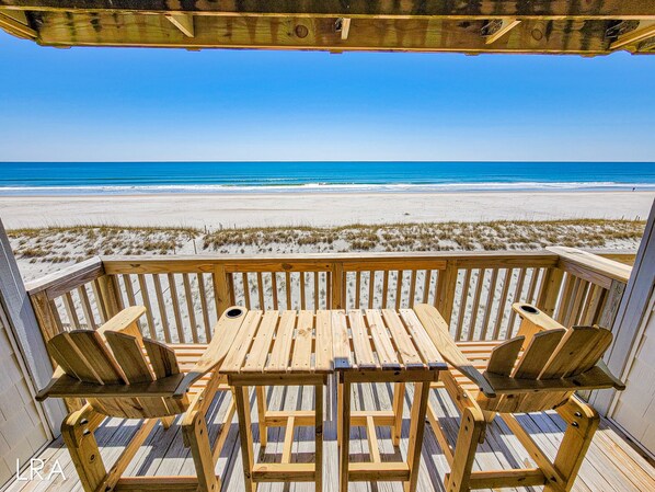 Una terraza de madera con mesa y sillas que da a una playa.