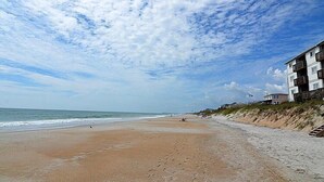 A beach with a sandy shore, ocean waves, and a building with balconies on the right.