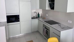 Una cucina moderna con mobili bianchi, forno integrato, lavello e piano di lavoro in marmo.