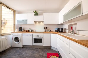 A compact kitchen with white cabinets, a wooden countertop, a washing machine, an oven, and a microwave. - BSH - Beaune Rousseau - Parking included (Beaune)
