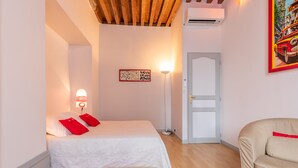 A bedroom with a bed, a red rug, a potted plant, a sofa, a wall-mounted lamp, and a door. - BSH - Beaune Rousseau - Parking included (Beaune)