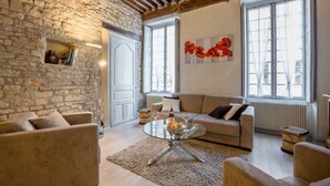Una sala de estar acogedora con pared de piedra, techo de madera, un sofá, una mesa de centro de vidrio y un ventanal con vistas.