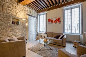 A cozy living room with a stone wall, a wooden ceiling, a sofa, a glass coffee table, and a large window with a view. - BSH - Beaune Rousseau - Parking included (Beaune)