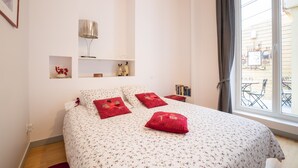 Un dormitorio con cama, mesita de noche, lámpara y ventana con vista al exterior.