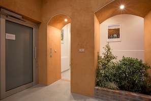 A hallway with a glass door, a brick planter with greenery, and a framed picture on the wall.