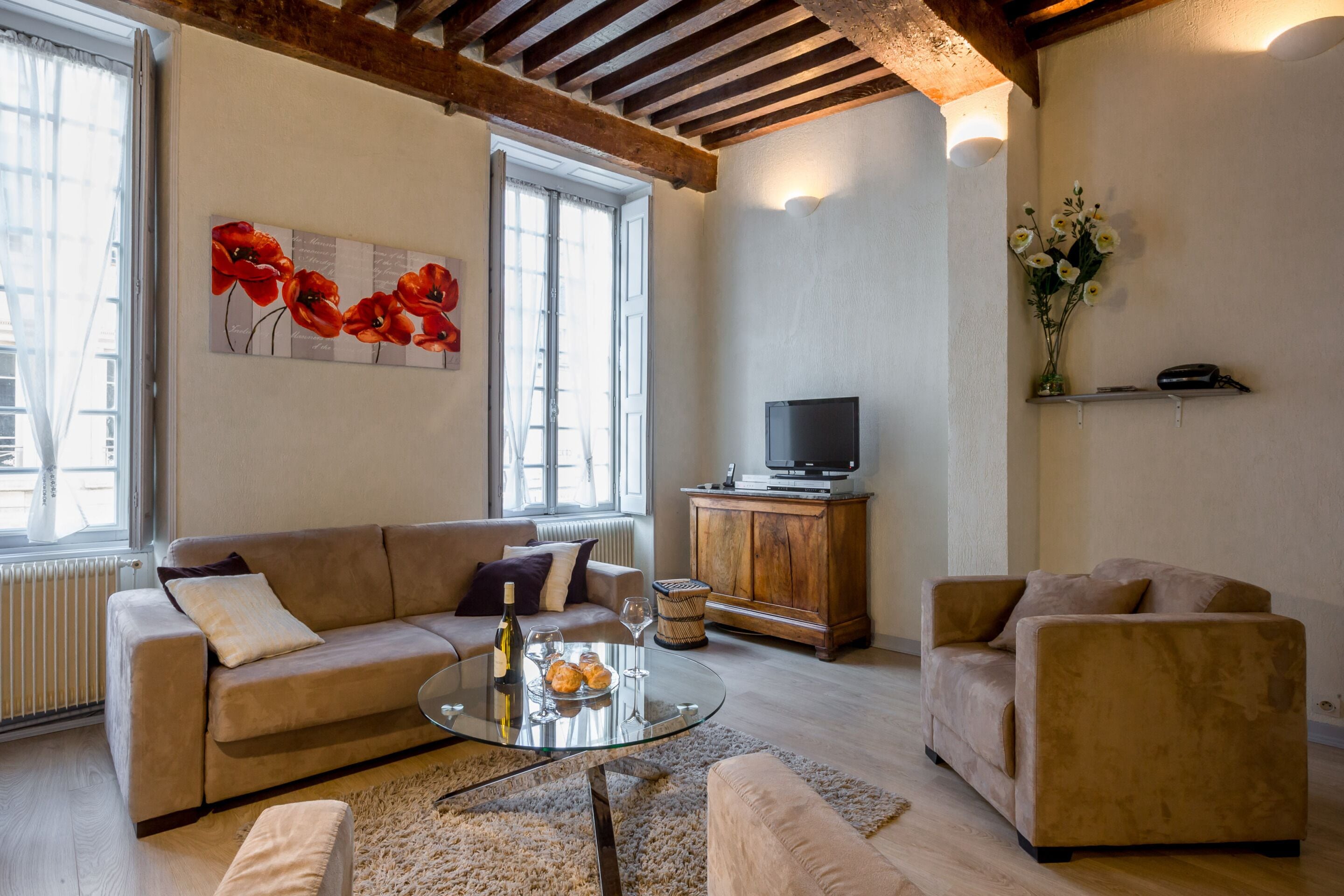 Un salon comprenant un canapé, un fauteuil, une table basse en verre et un téléviseur posé sur un meuble en bois.