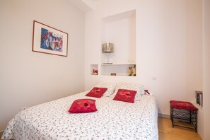 A bedroom with a bed, pillows, a framed picture, a lamp, and a small table.