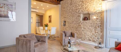 A cozy living room with a stone wall, two sofas, a glass coffee table, and a dining area in the background.