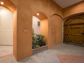 An interior hallway with a rustic design, featuring a wooden door and a brick planter with greenery.