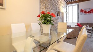 A modern living room with a glass-top dining table, white chairs, a stone wall, and a wooden ceiling. - BSH - Beaune Rousseau - Parking included (Beaune)