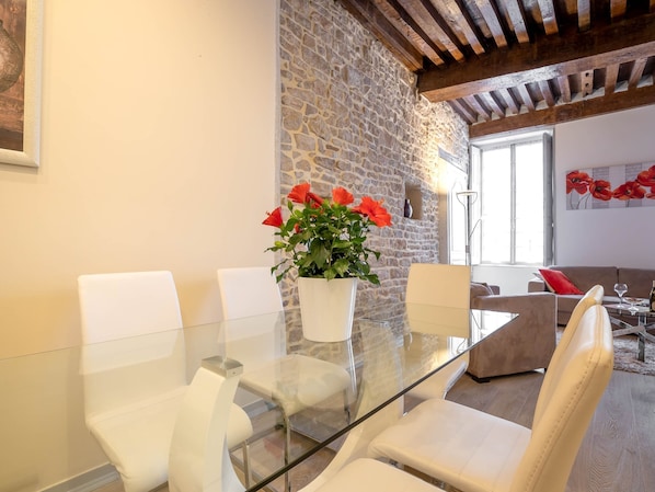 A modern living room with a glass-top dining table, white chairs, a stone wall, and a wooden ceiling. - BSH - Beaune Rousseau - Parking included (Beaune)