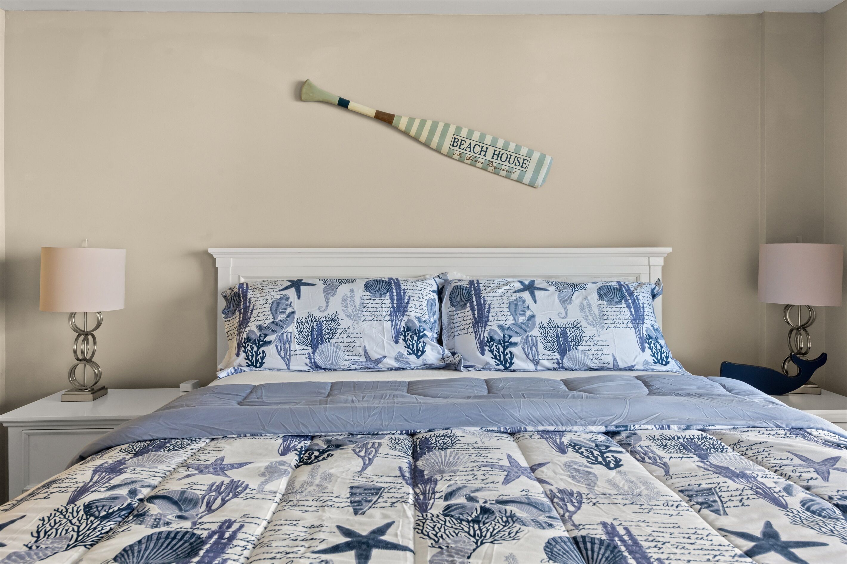 Une chambre à coucher avec un lit agrémenté d’une couvre-lit aux motifs marins bleus et blancs, deux lampes de chevet et un objet décoratif fixé au mur.