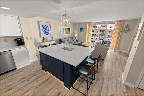 A modern kitchen with a central island, bar stools, and a dining area with a sofa. - N Hampton 907 in Kingston, Oceanview, Pool, Beach (Myrtle Beach)