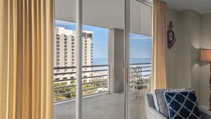 Ein Balkon mit Blick auf das Meer und Gebäude, ein Sessel mit gemustertem Kissen und eine an der Wand befestigte Uhr.