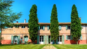 Un bâtiment à deux étages, doté d’un toit recouvert de tuiles, de volets verts et d’une cour intérieure avec un chemin pavé.