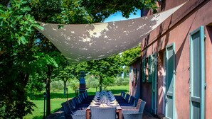 Un espace extérieur aménagé pour les repas, avec une table et des chaises, une pergola et un bâtiment en briques doté de volets.
