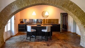 Une cuisine dotée d’une arche en pierre, de deux tabourets de bar, d’un îlot central et de luminaires suspendus.