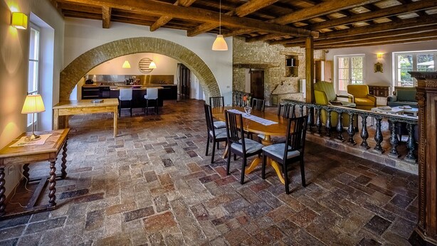 Une salle à manger spacieuse avec un sol en pierre, des poutres en bois au plafond et une grande table entourée de chaises.