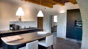 Une cuisine moderne dotée d’un îlot central, de luminaires suspendus et d’une cheminée en pierre.