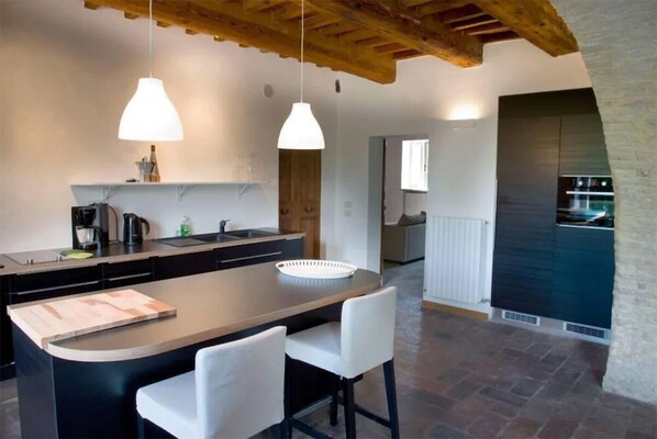 A modern kitchen with a central island, pendant lights, and a stone fireplace.