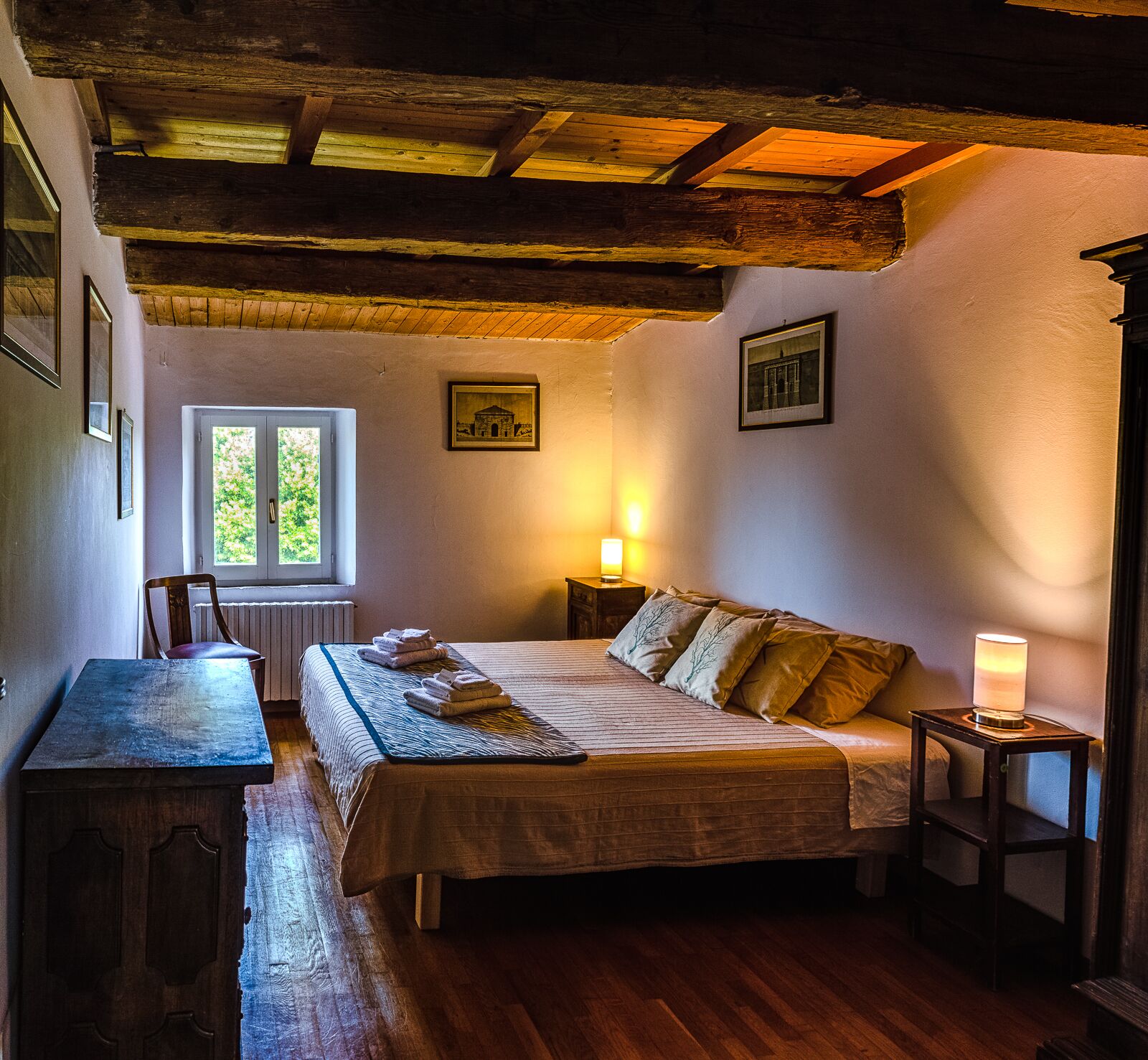 Une chambre confortable avec un plafond en bois, un lit avec des oreillers, une table de chevet avec une lampe et une fenêtre donnant sur un paysage verdoyant.