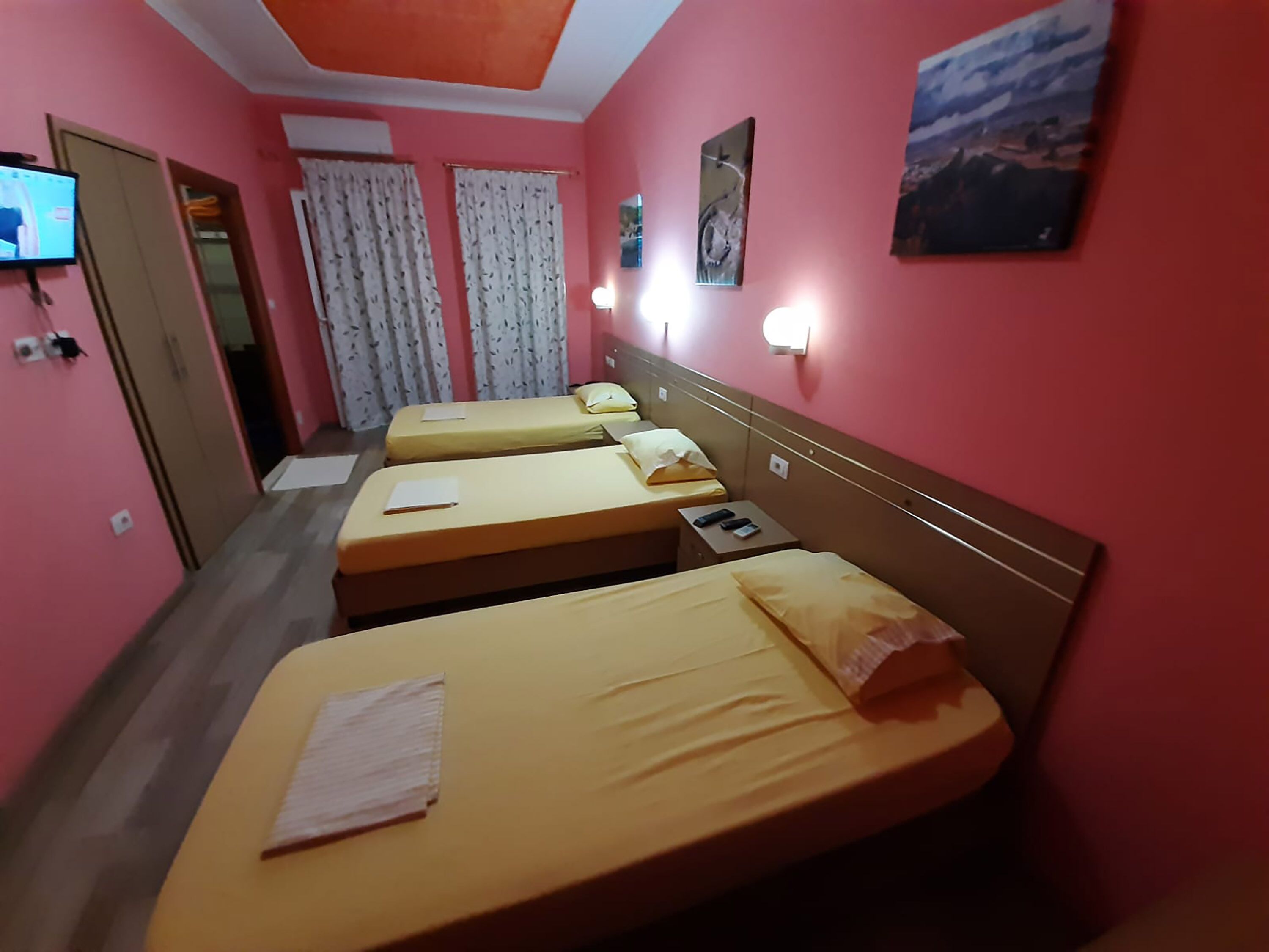 Una habitación de hotel con tres camas individuales, un televisor en la pared y un cuadro sobre las camas.