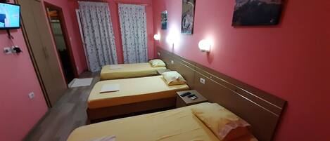 Una habitación de hotel con tres camas individuales, un televisor en la pared y un cuadro sobre las camas.