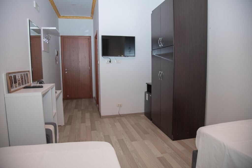 Habitación de hotel con cama, armario, escritorio, espejo y televisor montado en la pared.