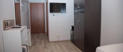 Habitación de hotel con cama, armario, escritorio, espejo y televisor montado en la pared.