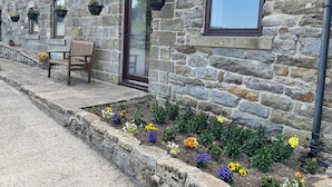 A stone building with a wooden bench, flower beds, and hanging flower baskets.