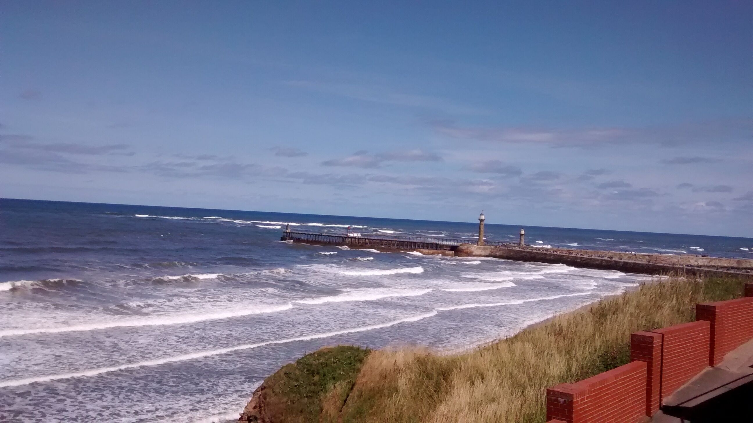 Vista costera con olas, un muelle y un faro.