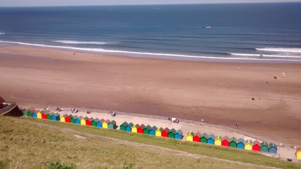 A beach with a row of colorful beach huts along the shoreline.