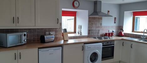 A modern kitchen with white cabinets, a microwave, a toaster, a dishwasher, a washing machine, a stove, and a red kettle.
