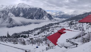 A snow-covered mountain landscape with a red-roofed building and a snow-covered path leading up to it. - Mountain Rover Auli (Joshimath)