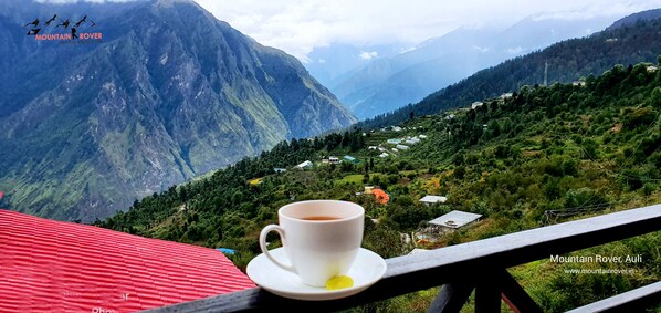 A cup of coffee on a table with a view of a mountainous landscape and small houses in the valley below.