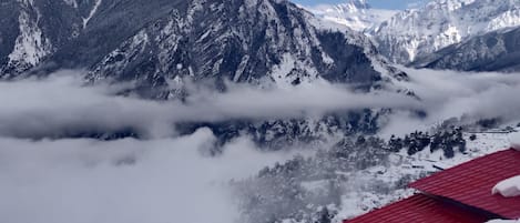 Paesaggio montuoso con cime innevate e un edificio con tetto rosso in primo piano.