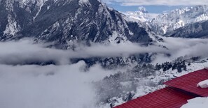 A mountainous landscape with snow-covered peaks and a red-roofed building in the foreground. - Mountain Rover Auli (Joshimath)