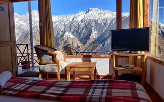 A room with a bed, a chair, a small table, a television, and a view of snow-covered mountains.