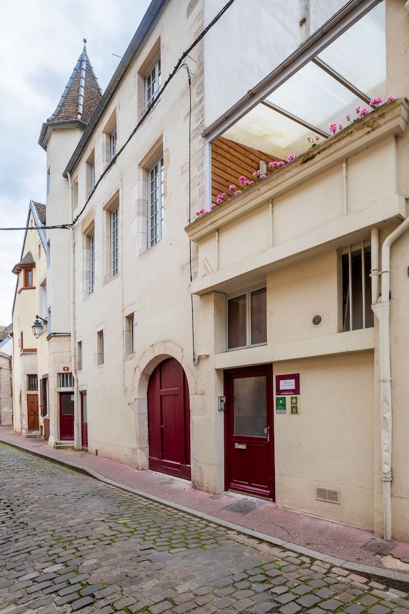 Un bâtiment historique avec une porte rouge, un balcon orné de fleurs et une rue pavée.