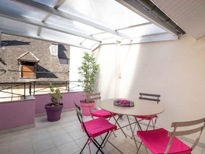 Un balcón con una mesa y sillas, plantas en macetas y vistas a edificios cercanos.