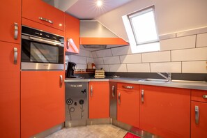 Una cocina moderna con armarios color naranja, electrodomésticos de acero inoxidable y una ventana sobre el fregadero.