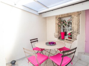 A small patio with a round table and four chairs, a window with flowers, and a door.
