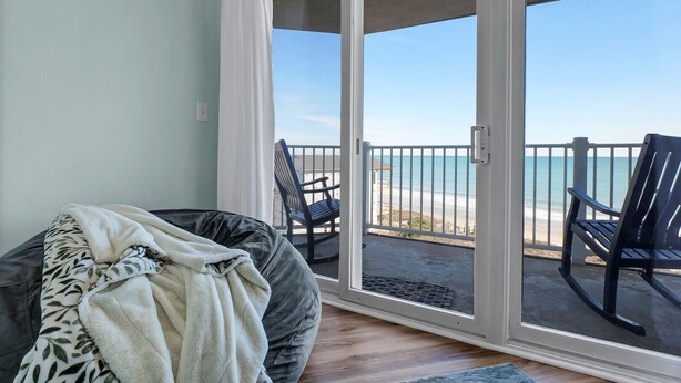 Una habitación con una cama, una silla y vistas a la playa a través de un ventanal corredizo.