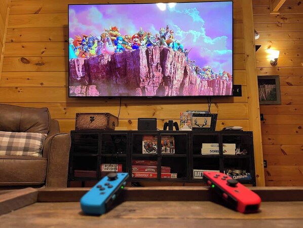 A living room with a television mounted on the wall, a brown leather couch, and a wooden cabinet with various board games.